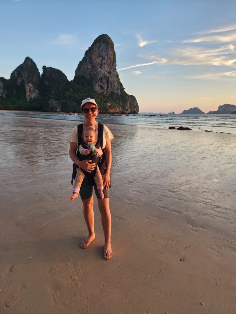 Mum carrying a young child in a baby carrier while travelling on the beach in thailand