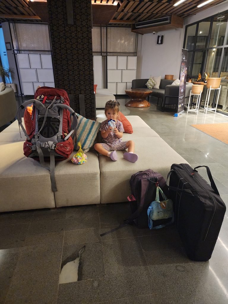 small child with a yogurt and bags and cot as they've arrived in a new country