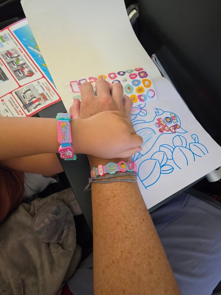 Young child keeping entertained during a long-haul flight making bracelets and drawing with her mum