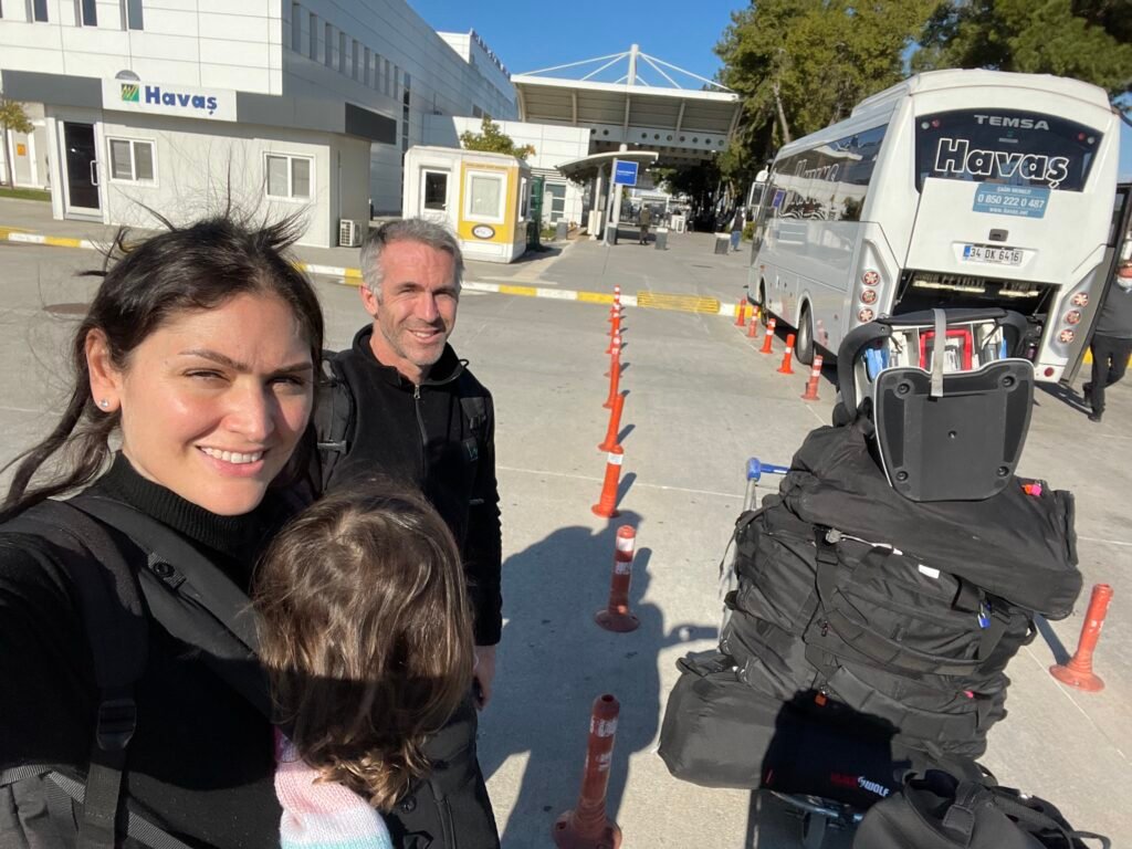 mum and dad waiting to board a bus with all of their suitcases and child in a baby carrier